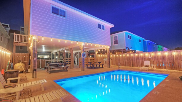 A backyard with a swimming pool, wooden deck chairs, and a covered patio area. - Salty Peach by AvantStay | Private Pool, New Decor (Port Aransas)