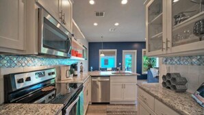 A modern kitchen with stainless steel appliances, white cabinetry, and a blue accent wall. - Pool, Walk to Old Town + Eateries, Nightlife, Shopping | Rock N Reelby AvantStay (Port Aransas)