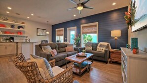 A living room with a dark blue wall, a ceiling fan, a coffee table, and a sofa with cushions. - Pool, Walk to Old Town + Eateries, Nightlife, Shopping | Rock N Reelby AvantStay (Port Aransas)