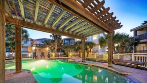 A pool area with a wooden pergola overhead, palm trees, and a building in the background. - Pool, Walk to Old Town + Eateries, Nightlife, Shopping | Rock N Reelby AvantStay (Port Aransas)