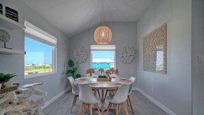 A dining area with a round table set for six, surrounded by white chairs with wooden legs. - Outdoor Lounge w/ Bar Swing Seats, Near Nature Preserve | Blutopia by AvantStay (Port Aransas)