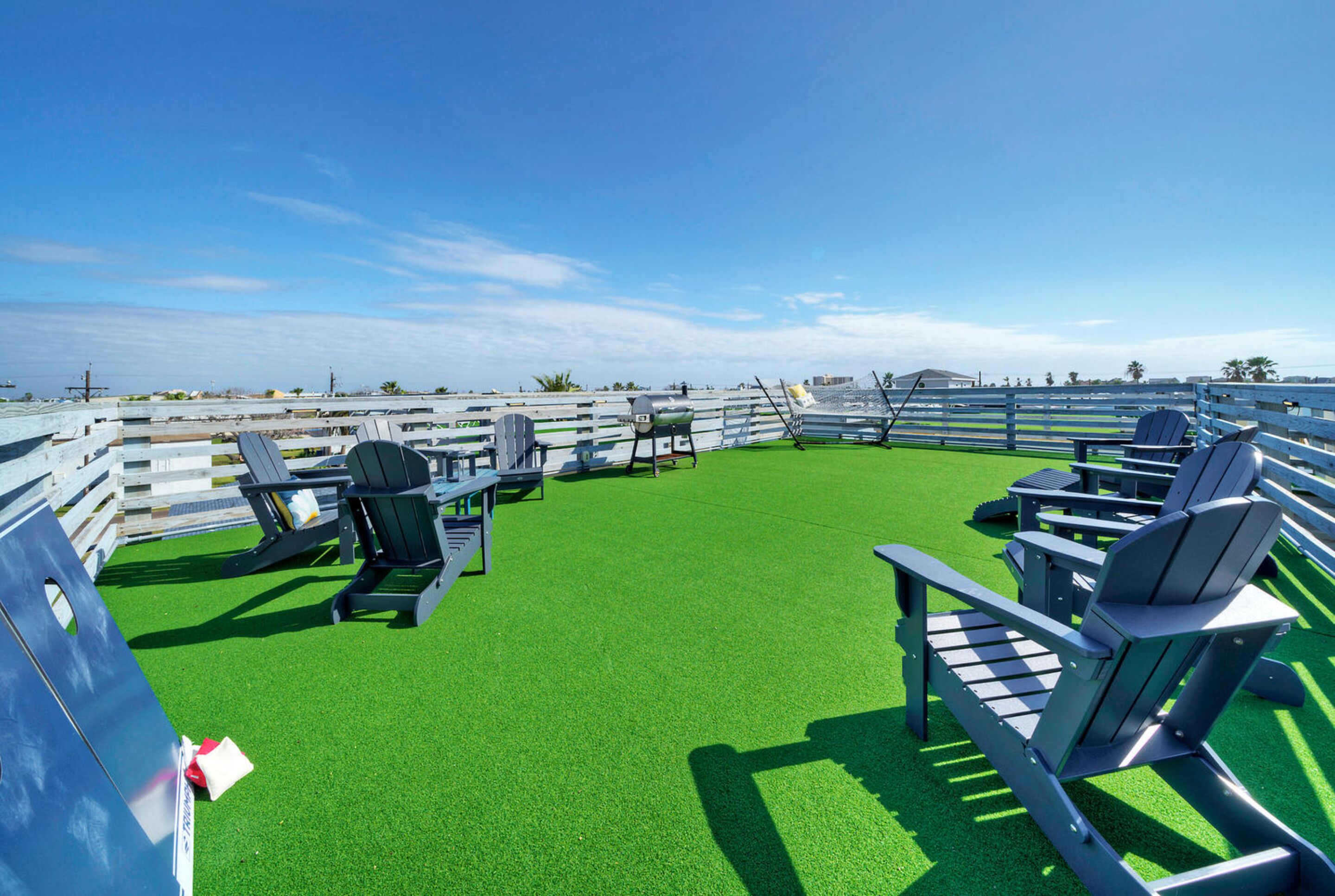 A deck with green artificial turf, outdoor furniture, and a view of the ocean.
