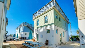 A two-story building with a patio area, outdoor seating, and a small garden. - Stella Maris by AvantStay | Rooftop View + Pool (Port Aransas)