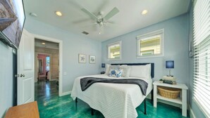 A bedroom with a bed, bedside tables, a ceiling fan, and a view of the hallway. - Stella Maris by AvantStay | Rooftop View + Pool (Port Aransas)