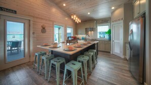 Una cocina moderna con paredes de madera, una isla central con taburetes, electrodomésticos de acero inoxidable y vistas a la playa.
