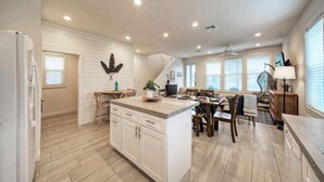 A spacious kitchen with a large island, wooden flooring, and a dining area with a table and chairs. - Newly Built, Pool, Walk to Old Town Eats+Marina | Shorely Goodness by AvantStay (Port Aransas)