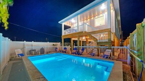 Uma casa de dois andares com piscina, espreguiçadeiras e um espaço de varanda coberto.
