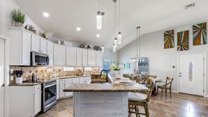 Une cuisine spacieuse avec des meubles blancs, un îlot central et un coin repas doté de chaises en bois.