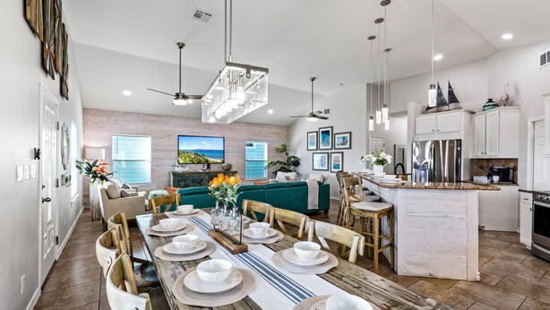 Une cuisine spacieuse avec un îlot central, une table à manger en bois pouvant accueillir six personnes et un coin salon confortable avec une grande télévision et des sièges confortables.