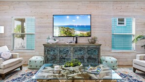 Un salon avec un mur en bois, un téléviseur à écran plat, une table basse en verre et deux poufs.