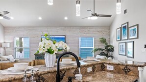 Une cuisine moderne dotée de plans de travail en granit, d’éviers en acier inoxydable et d’un robinet noir. On peut y admirer des fleurs décoratives sur le plan de travail et un ventilateur de plafond au-dessus.