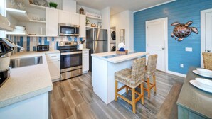 A modern kitchen with white cabinetry, stainless steel appliances, and a blue accent wall. - Pool | 1 Block to Alister + Old Town + Eateries | Bluegrass Breeze by AvantStay (Port Aransas)
