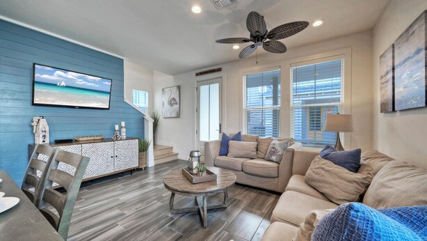 A living room with a blue accent wall, a ceiling fan, a sofa, a coffee table, and a dining area with chairs. - Pool | 1 Block to Alister + Old Town + Eateries | Bluegrass Breeze by AvantStay (Port Aransas)
