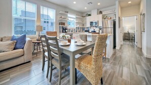 A modern kitchen with white cabinets, stainless steel appliances, and a dining area with wicker chairs and a table. - Pool | 1 Block to Alister + Old Town + Eateries | Bluegrass Breeze by AvantStay (Port Aransas)