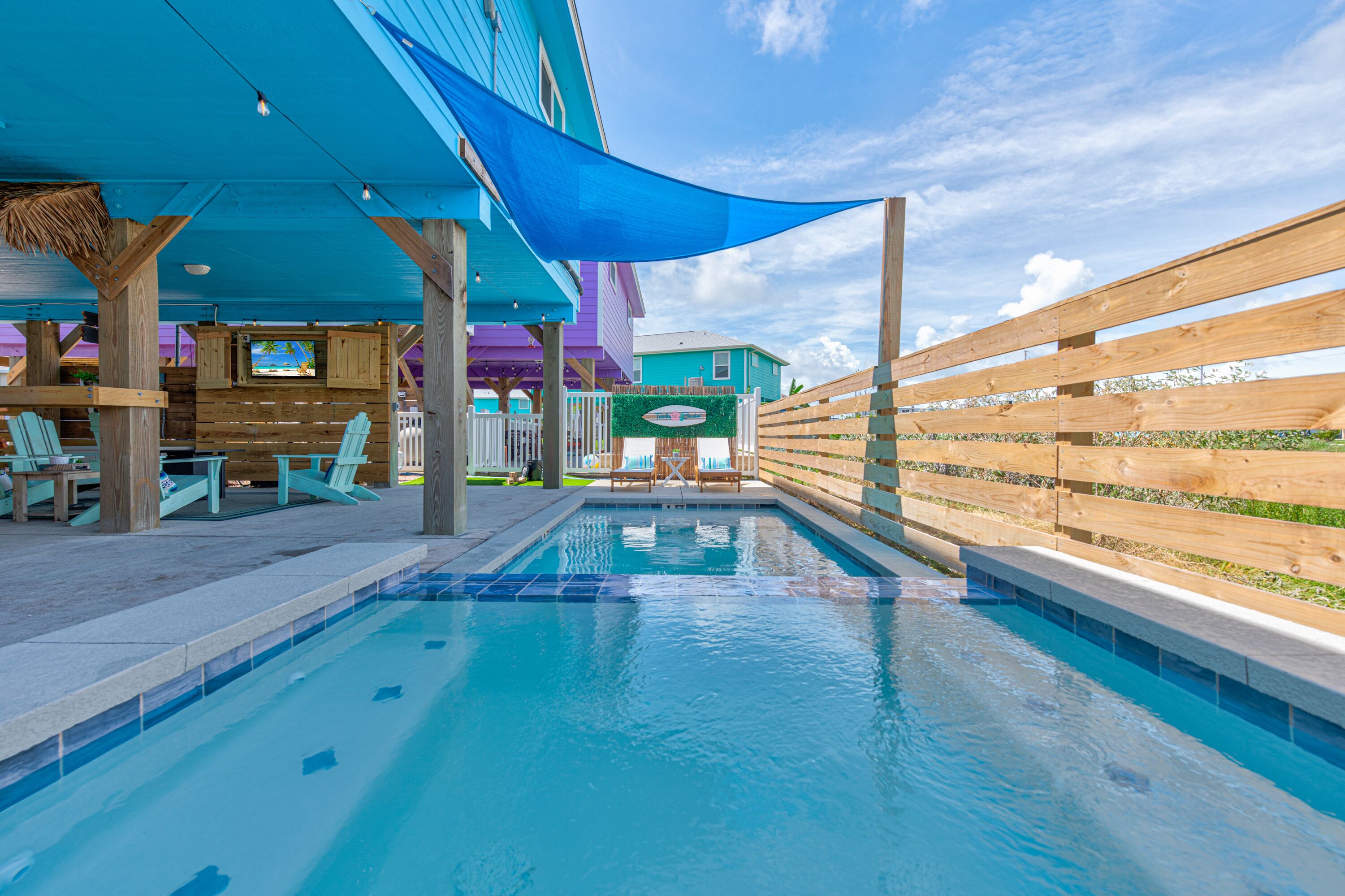 A pool area with wooden deck chairs, a pool, and a covered seating area with a blue canopy.
