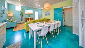 Un coin repas avec une table dressée pour quatre personnes, un canapé vert, un divan bleu et un ventilateur de plafond.
