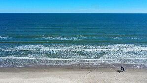 Une plage avec des vagues, un ciel dégagé et une personne qui se promène.