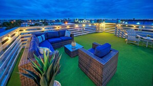 Un espace extérieur aménagé avec des meubles en osier et offrant une vue sur la ville au crépuscule.