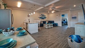 A modern kitchen with a central island, a dining area with a wooden table, and a living room with a sofa and a bed.