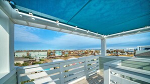 A balcony with a view of a coastal town, featuring a wooden deck and white railings.