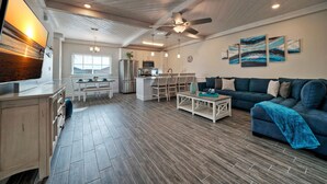 A spacious living area with a dark blue sofa, a coffee table, and a kitchen area with a refrigerator, microwave, and dining table.