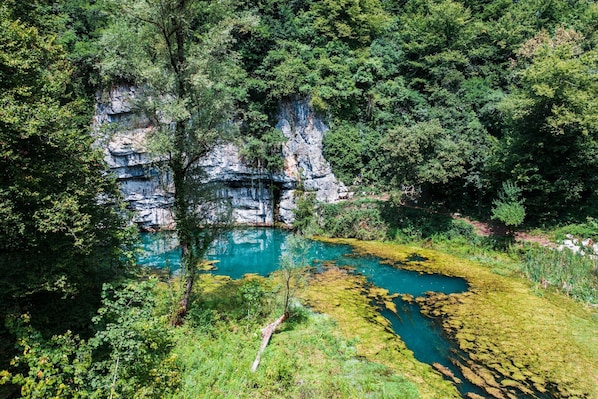 A natural landscape with a clear water body surrounded by dense greenery and rocky cliffs. - Pool Chalet Adonis w/ Panoramic Views (Semič)