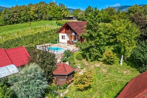 A house with a swimming pool, surrounded by lush greenery and a fenced garden.