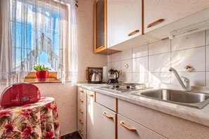 A kitchen with a sink, stove, and window with curtains.