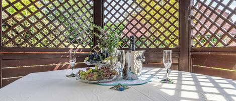 A table set for two with a white tablecloth, a pitcher, a bowl of fruit, and two wine glasses.