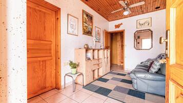 Una habitación con techo de madera, ventilador de techo, sofá, una mesita con una planta y alfombra a cuadros.