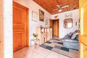 A room with a wooden ceiling, a ceiling fan, a sofa, a small table with a plant, and a checkered rug.