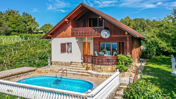 Eine zweistöckige Holzhütte mit Balkon, Schwimmbecken und einem Kiesweg zum Eingang.