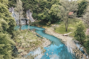 A river winding through a forested area with a rocky cliff and a small building near the water. - Pool Chalet Adonis w/ Panoramic Views (Semič)