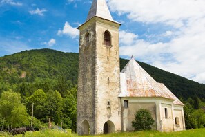A historic stone church with a bell tower and a smaller building with a tiled roof, surrounded by lush greenery and hills. - Pool Chalet Adonis w/ Panoramic Views (Semič)