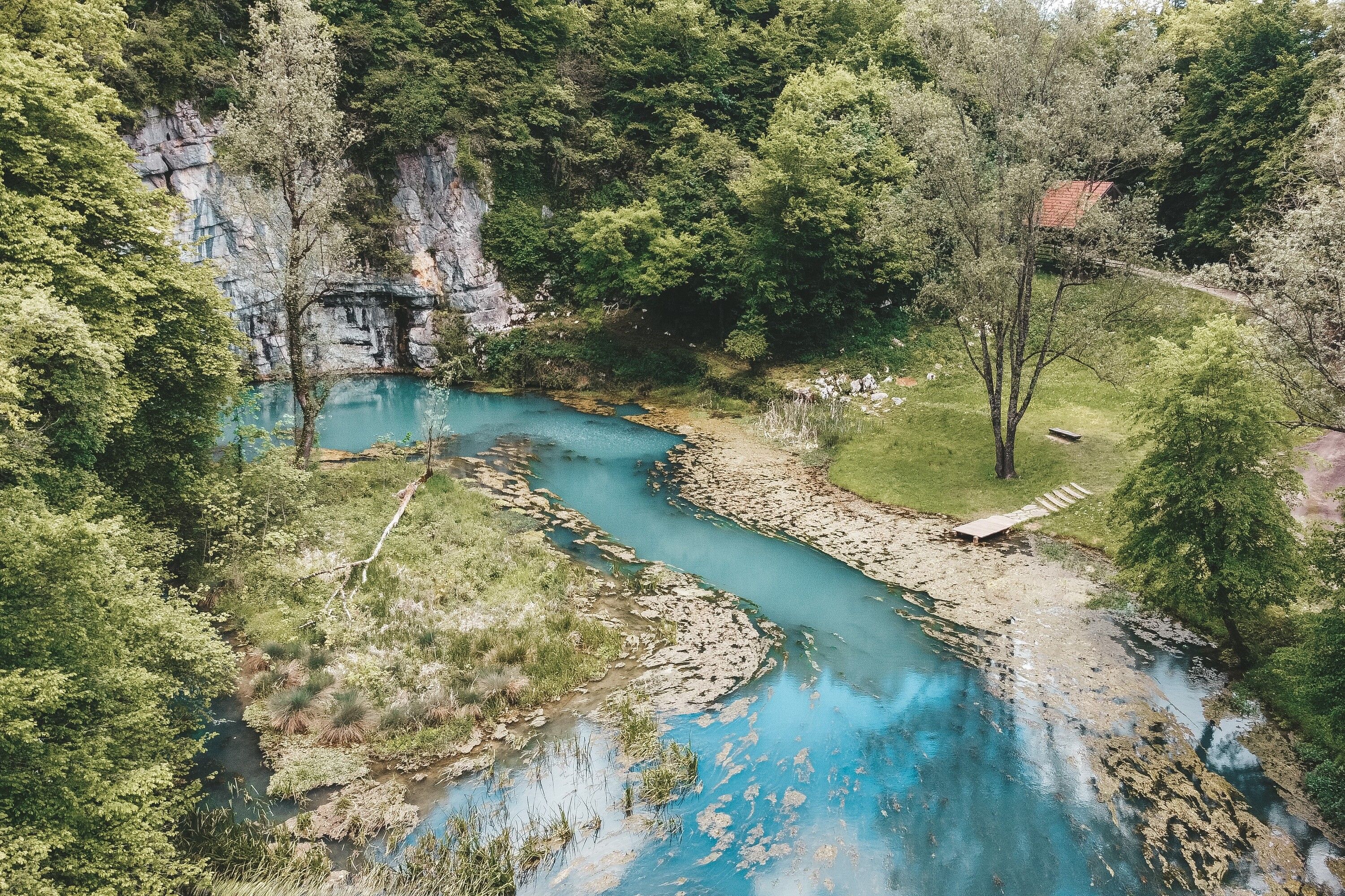 Un río serpentea por una zona boscosa con un acantilado rocoso y un pequeño edificio cerca del agua.