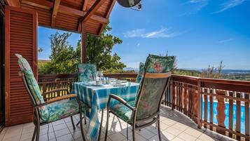 Un espacio de estar al aire libre cubierto con mesa y sillas, piscina al fondo y vistas al paisaje.
