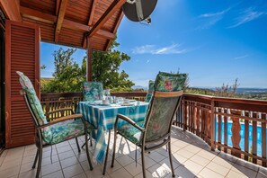 A covered outdoor seating area with a table and chairs, a pool in the background, and a view of the landscape.