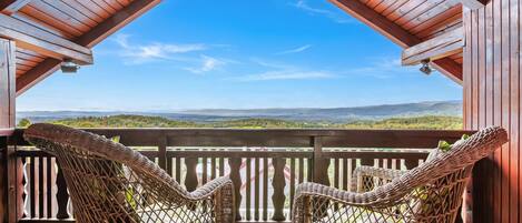 A wooden balcony with wicker chairs and a view of a green landscape.