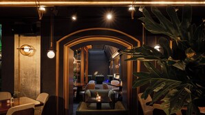 A restaurant with a cozy interior, featuring a central seating area with a table and chairs, and a large plant in the foreground. - REY Hotel Hanoi (Hanoi)