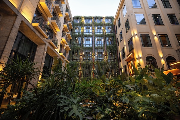 A multi-story building with balconies, a central atrium with dense foliage, and illuminated exterior lighting.