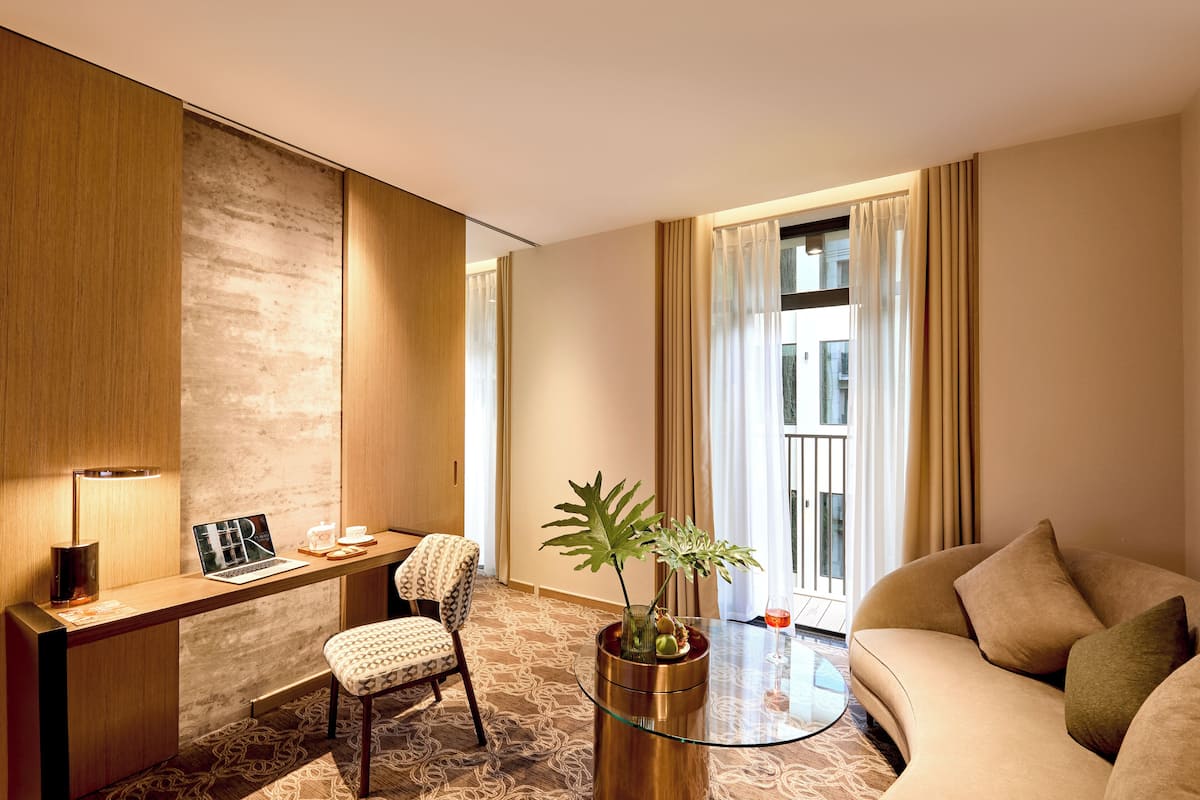 A modern hotel room with a wooden desk, a laptop, a chair, a sofa, a glass coffee table, and a potted plant.