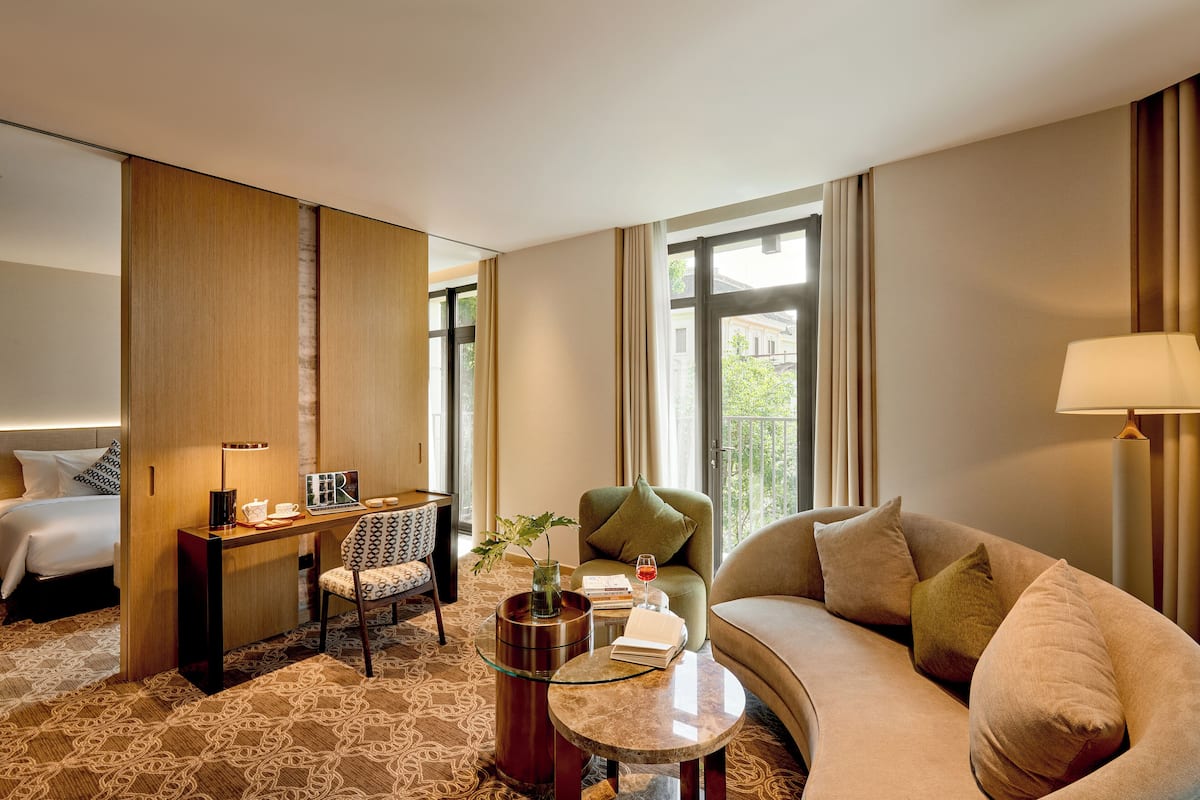 A hotel room with a bed, a sofa, a desk with a chair, a coffee table, and a window with curtains.