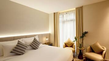 Une chambre d’hôtel avec un grand lit, deux tables de chevet, une lampe, une chaise et une petite table sur laquelle est posée une plante.