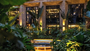 A lush indoor garden with a central water feature, surrounded by large windows and tropical plants. - REY Hotel Hanoi (Hanoi)