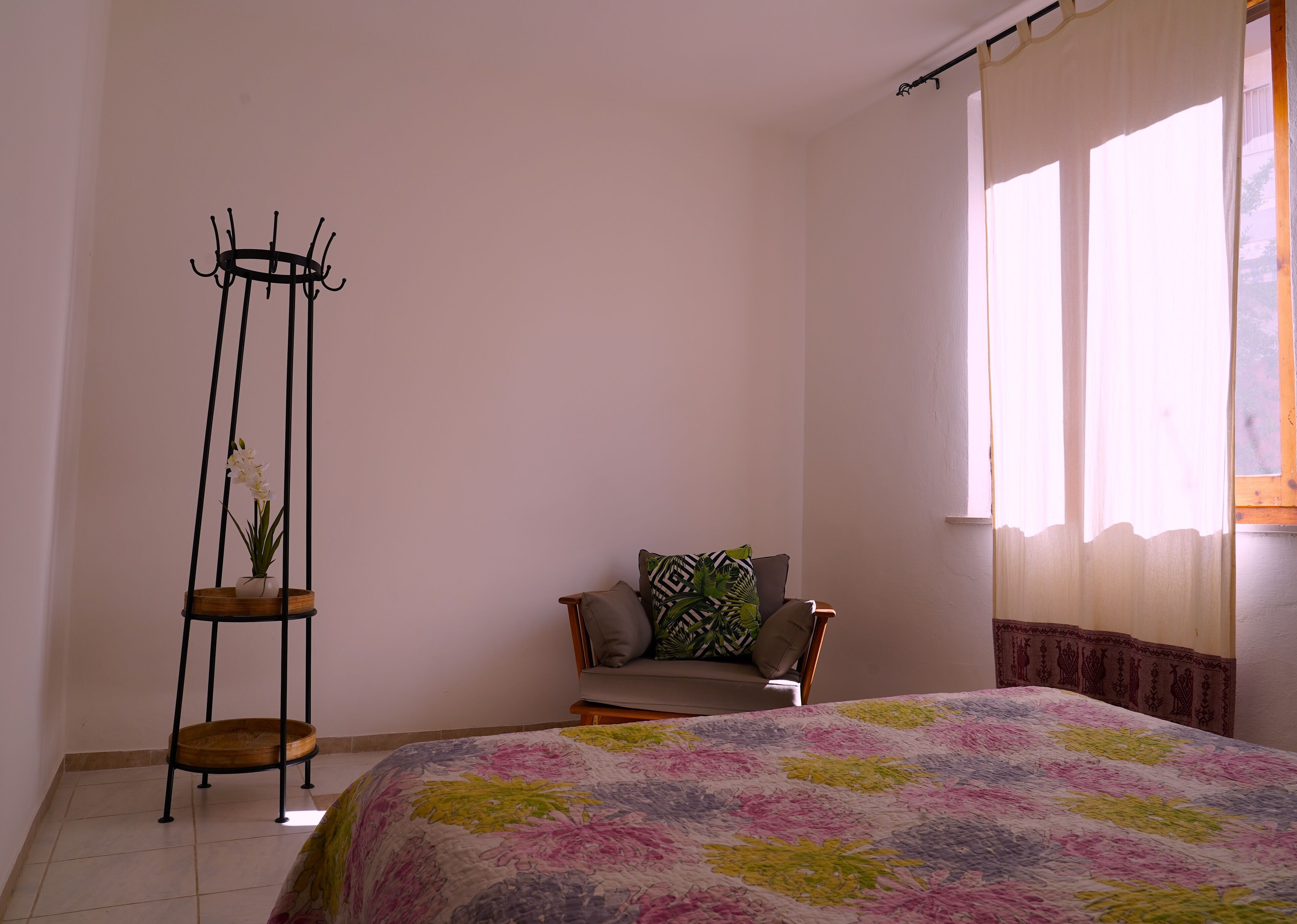 Een slaapkamer met een bed, een stoel, een kamerplant en een raam met gordijnen.