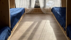 A small, wooden-roofed room with two beds, a window with sheer curtains, and a sloped ceiling. - Bakhmaro (Bakhmaro)