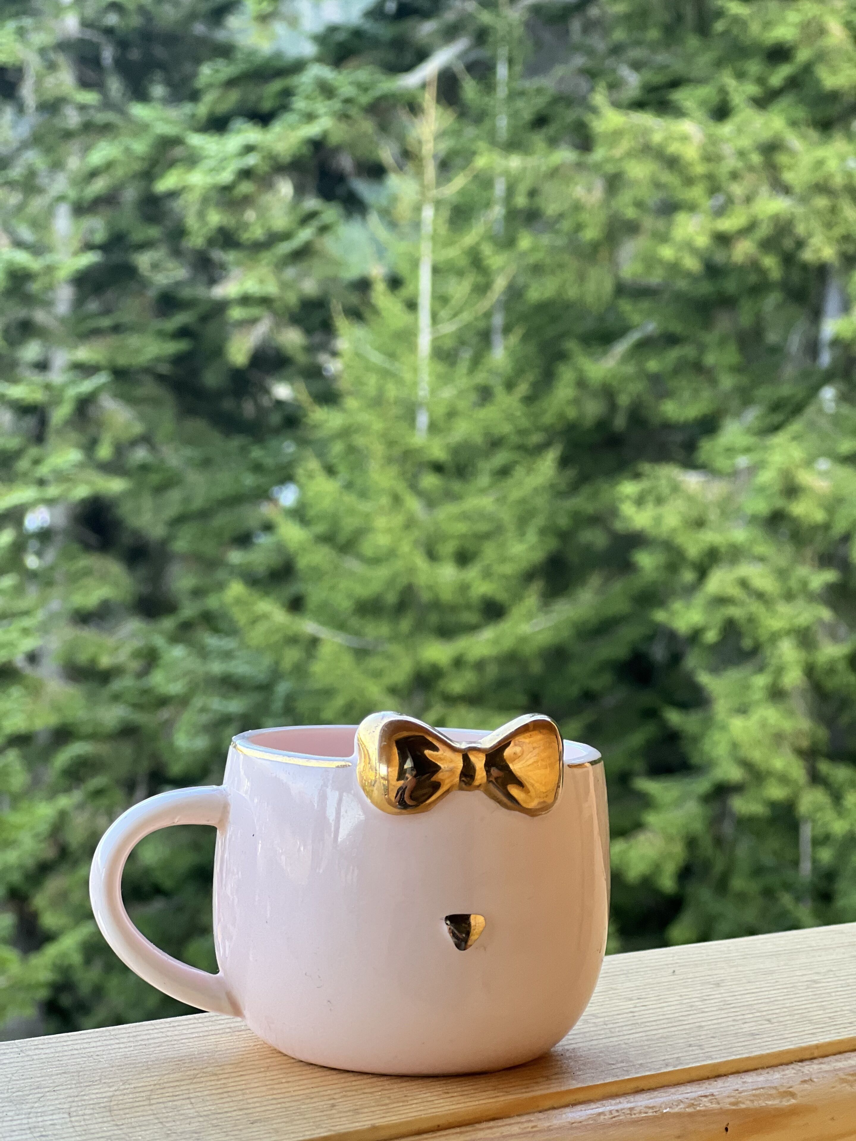 Una taza rosa con una pajarita dorada sobre una superficie de madera con un fondo de bosque.