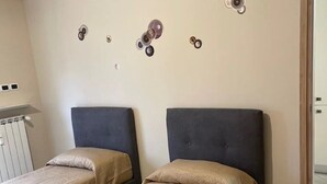A hotel room with two beds, beige bedding, a radiator, and a wall-mounted security camera. - Casamagnolia, your home (Cernusco sul Naviglio)
