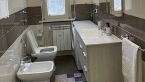 A compact bathroom with a toilet, bidet, and sink, a mirror, and a window with a decorative screen. - Casamagnolia, your home (Cernusco sul Naviglio)