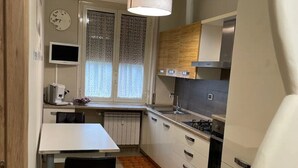 A compact kitchen with a dining table, a built-in oven, and a window with patterned curtains. - Casamagnolia, your home (Cernusco sul Naviglio)